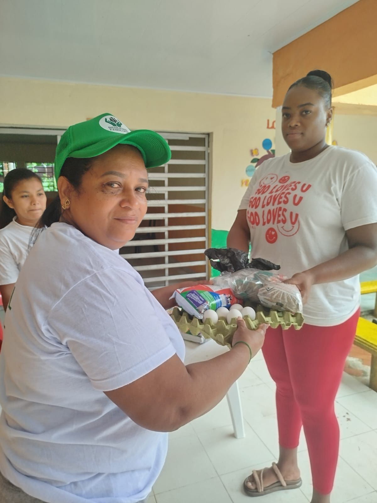 Integrante de Manos Amigas con gorra institucional entregando mercado a beneficiaria con expresión cálida de solidaridad